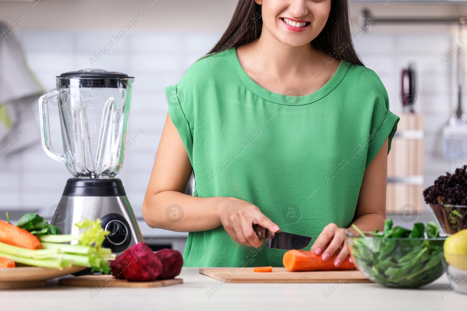 Photo of Young woman preparing tasty healthy smoothie at table in kitchen