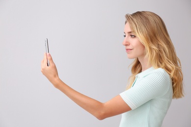 Photo of Young woman unlocking smartphone with facial scanner on grey background. Biometric verification
