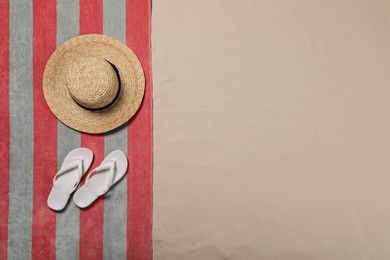 Beach towel, flip flops and hat on sand, top view. Space for text