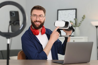 Photo of Smiling technology blogger recording video review about virtual reality headset at home