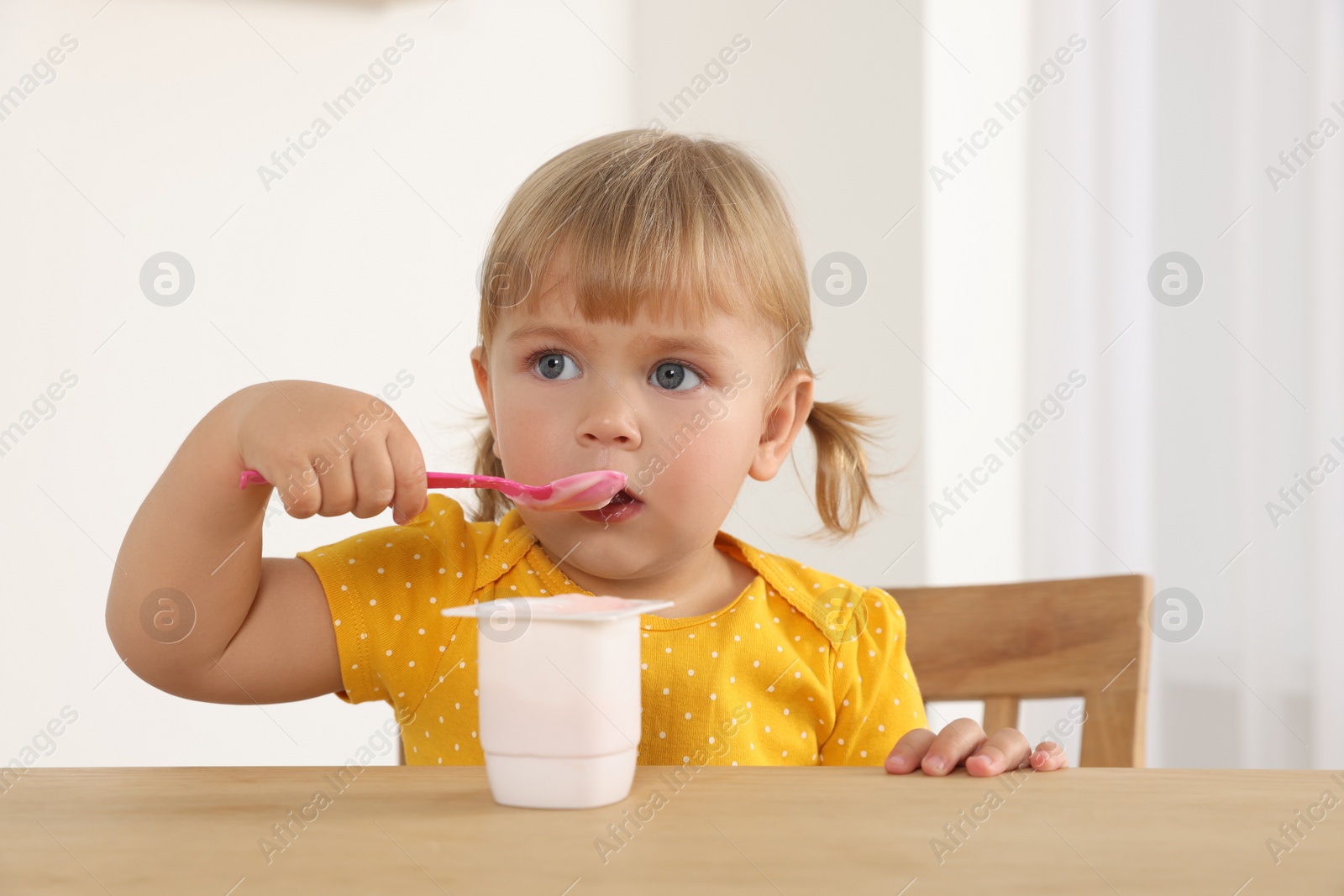 Photo of Cute little child eating tasty yogurt with spoon at wooden table indoors