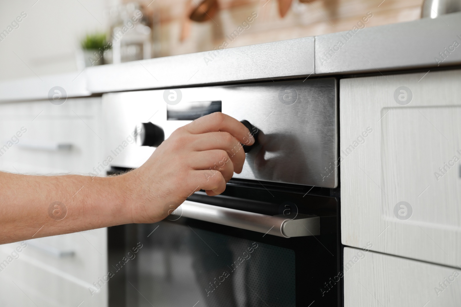 Photo of Man regulating cooking mode on oven panel in kitchen, closeup