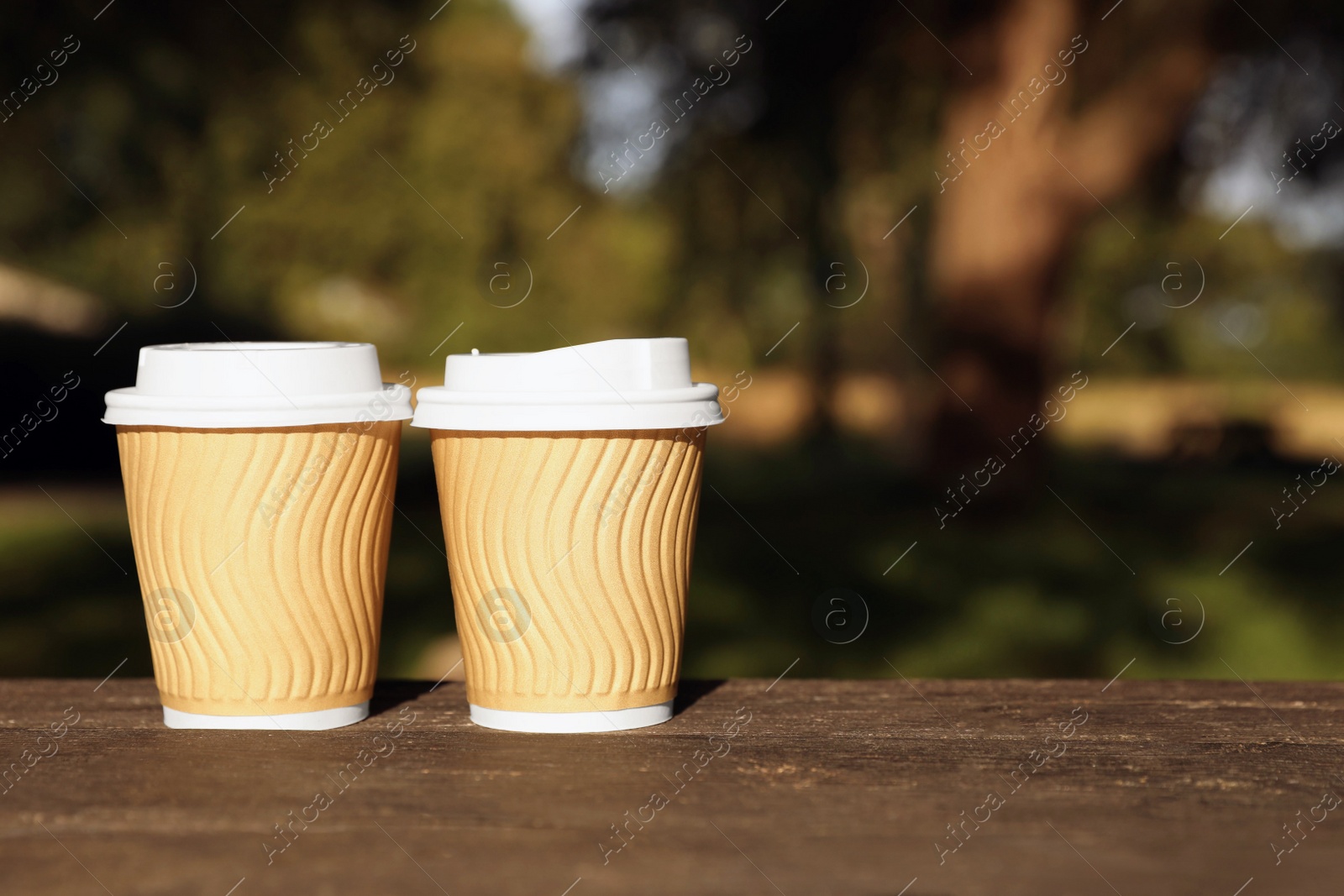 Photo of Paper cups on wooden table in park, space for text. Coffee to go