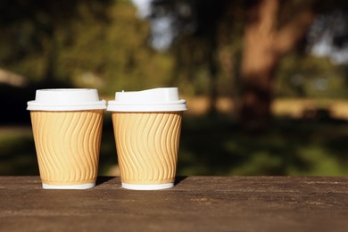 Photo of Paper cups on wooden table in park, space for text. Coffee to go