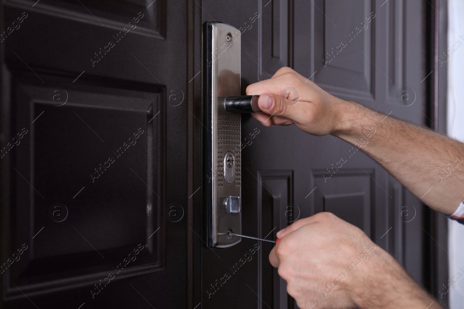 Photo of Handyman with screwdriver repairing door lock, closeup