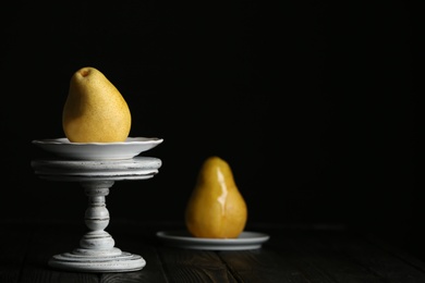 Photo of Stand with fresh ripe pear on table against dark background. Space for text