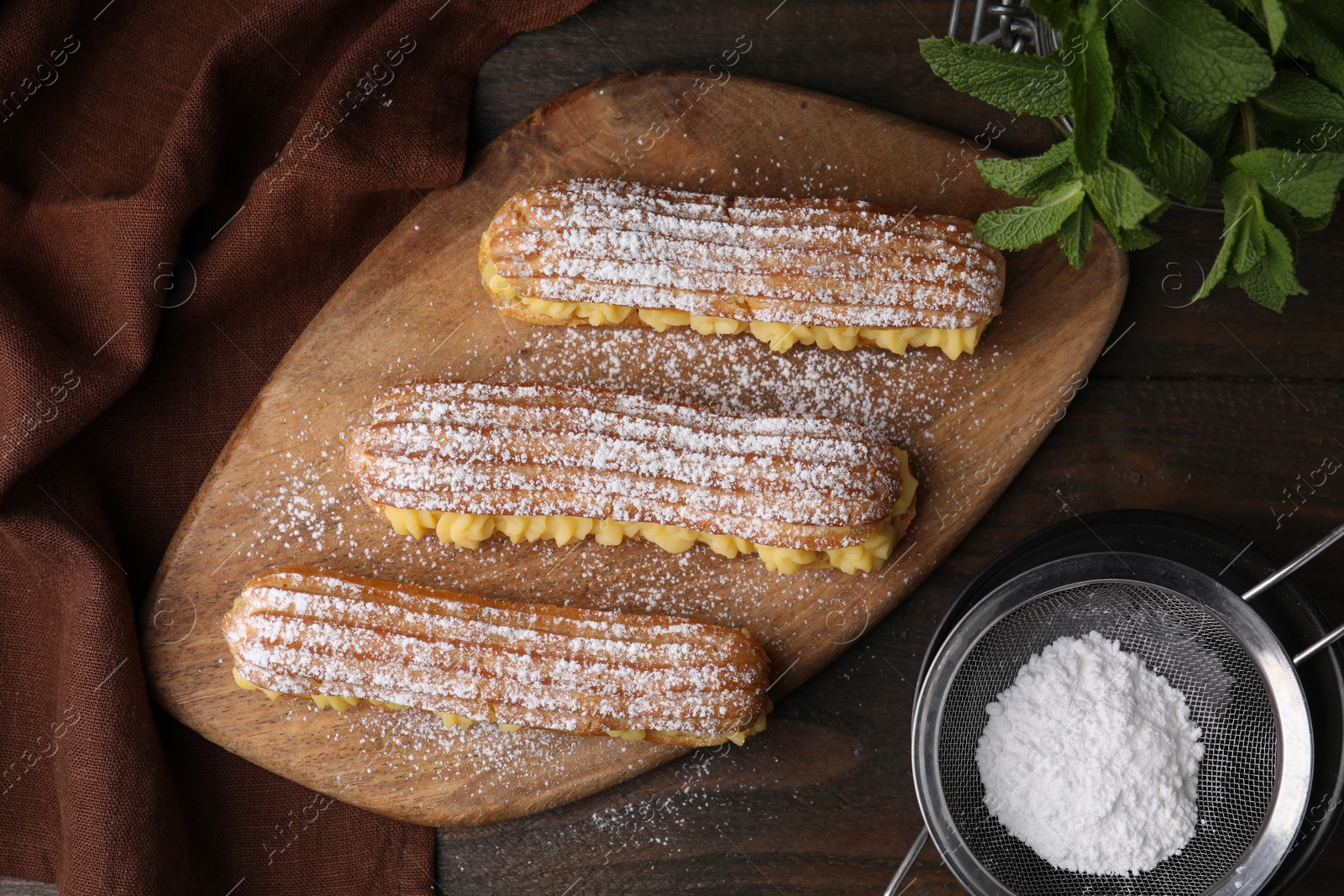 Photo of Delicious eclairs filled with cream, mint and powdered sugar on wooden table, top view