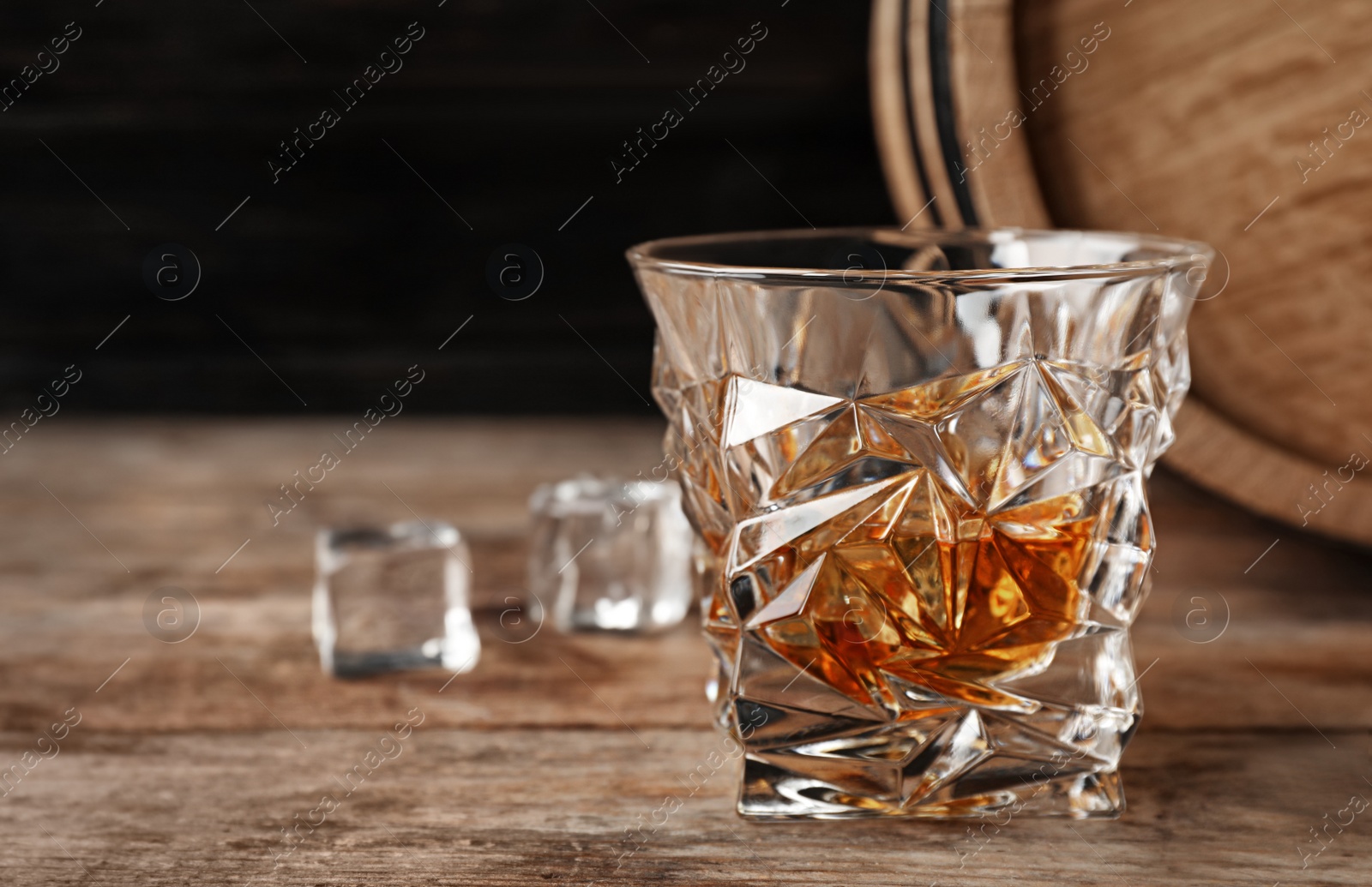 Photo of Golden whiskey in glass with ice cubes on wooden table. Space for text