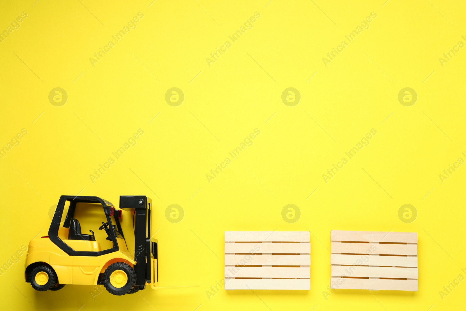 Photo of Toy forklift and wooden pallets on yellow background, flat lay. Space for text