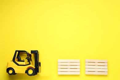 Photo of Toy forklift and wooden pallets on yellow background, flat lay. Space for text