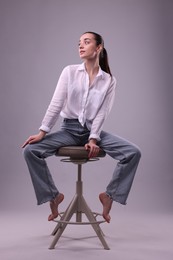 Portrait of beautiful young woman sitting on chair against light grey background