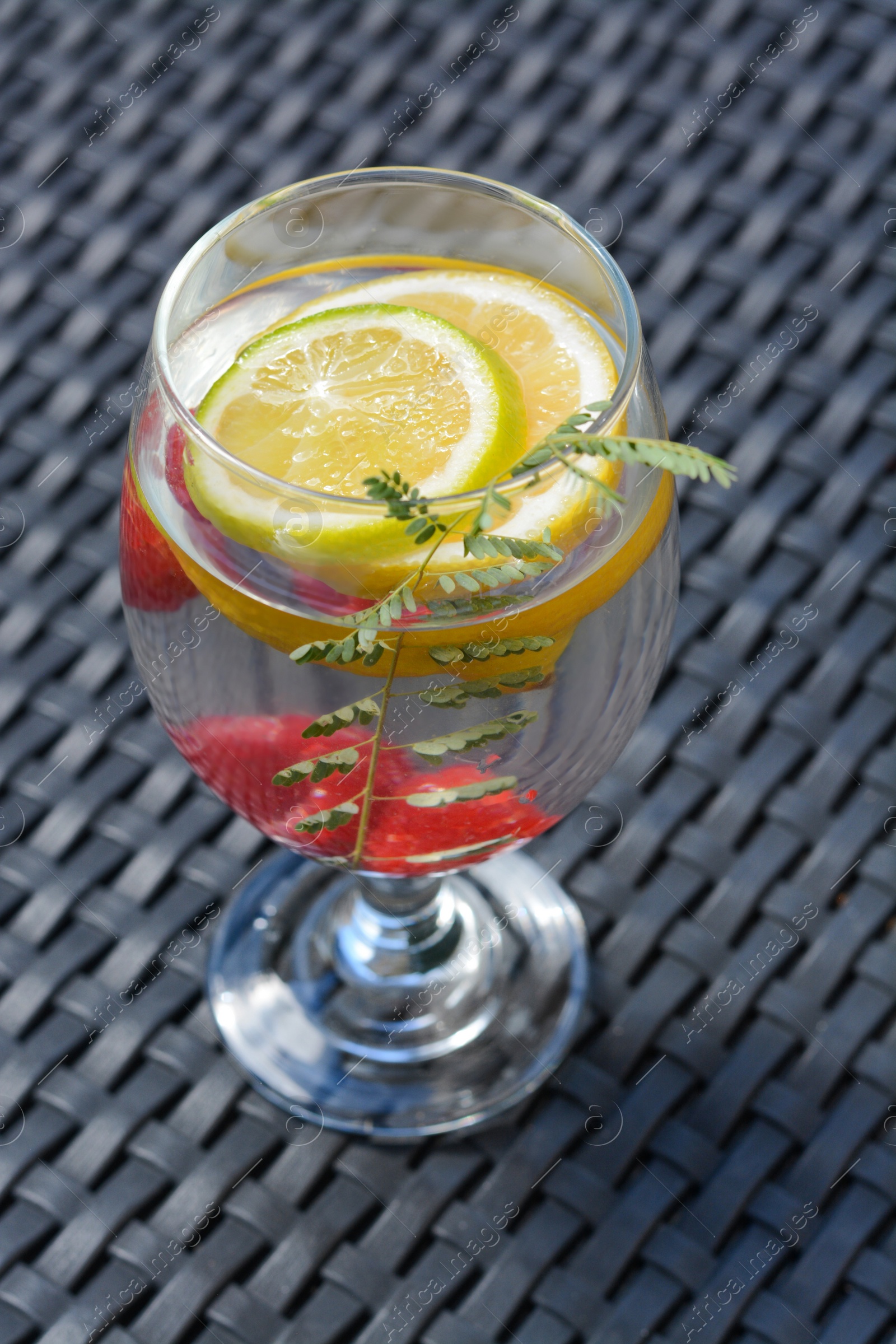 Photo of Delicious refreshing lemonade with raspberries on black rattan surface
