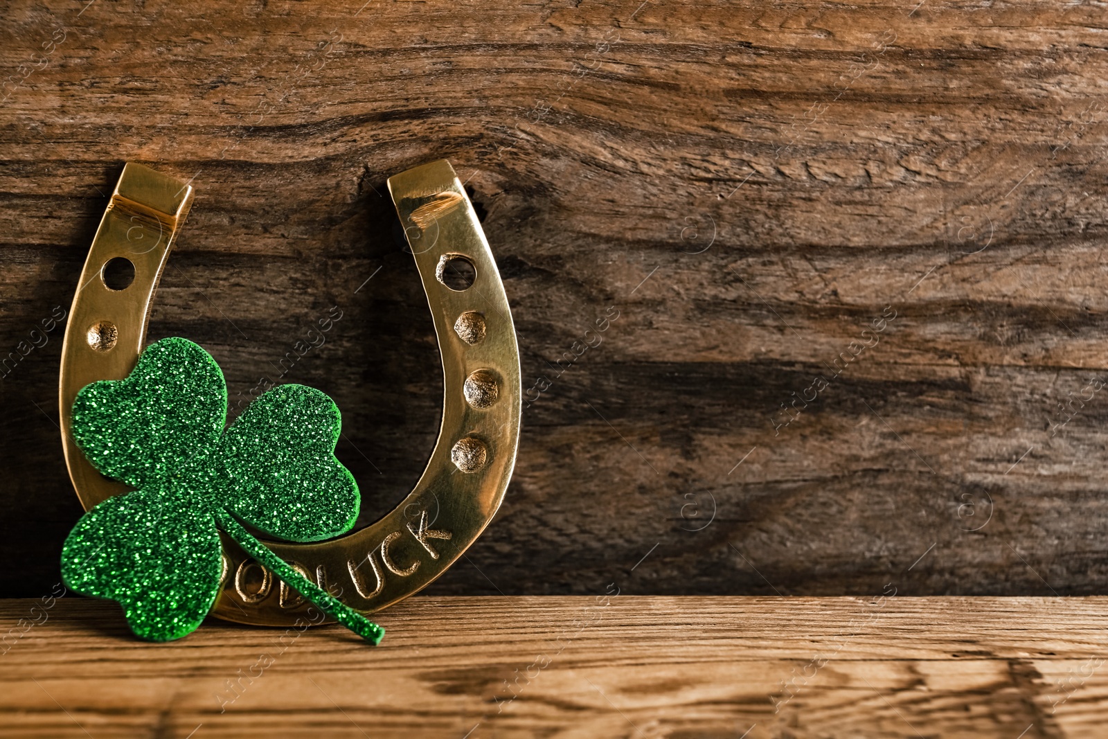 Photo of Golden horseshoe and decorative clover leaf on wooden background, space for text. Saint Patrick's Day celebration