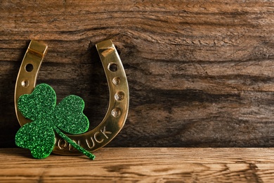 Golden horseshoe and decorative clover leaf on wooden background, space for text. Saint Patrick's Day celebration