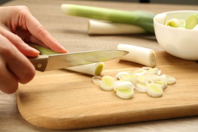 Woman cutting fresh raw leek at wooden table, closeup