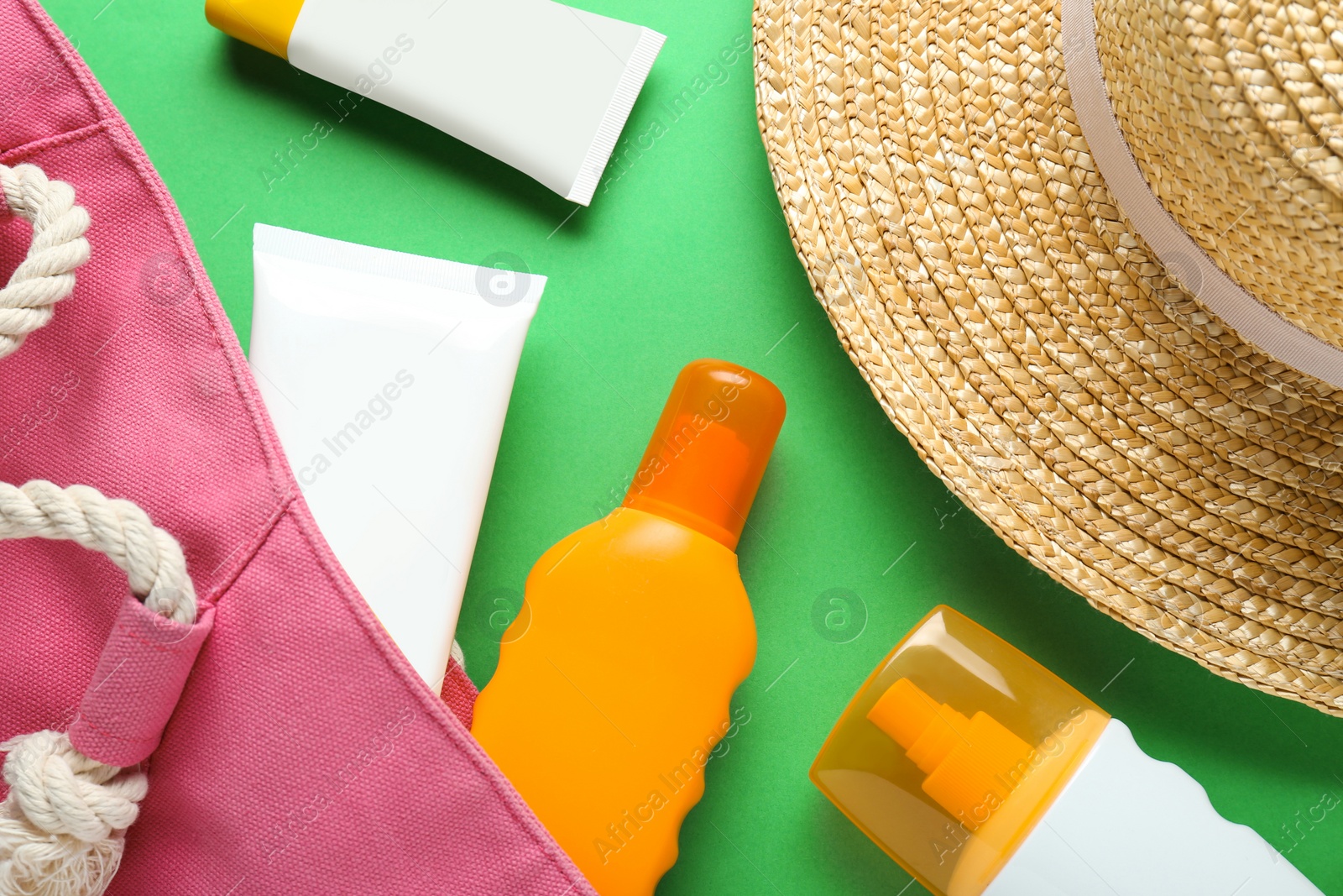 Photo of Suntan products, bag and straw hat on green background, flat lay