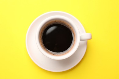 Fresh coffee in cup on yellow background, top view