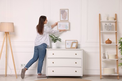 Woman hanging picture frame on white wall at home