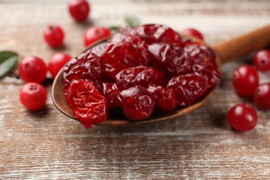 Photo of Tasty dried cranberries in spoon and fresh ones on rustic wooden table, closeup