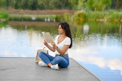 Photo of Young woman reading book on pier near lake