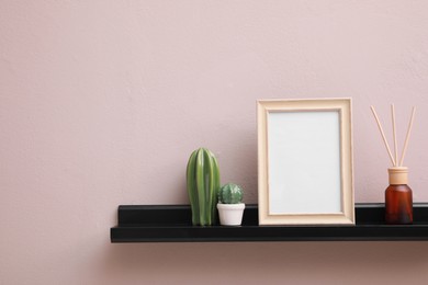 Photo of Empty photo frame, cactus figures and air reed freshener on shelf near pink wall, space for text