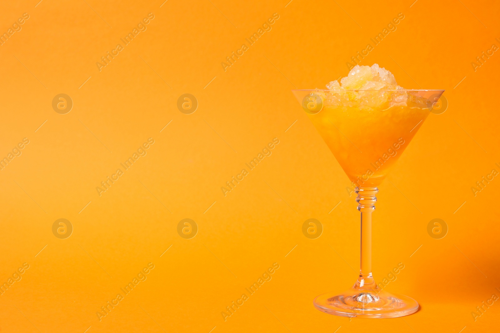 Photo of Shaving ice in martini glass on orange background, space for text