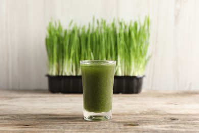 Wheat grass drink in shot glass on wooden table, closeup