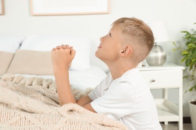 Photo of Boy with clasped hands praying near bed at home
