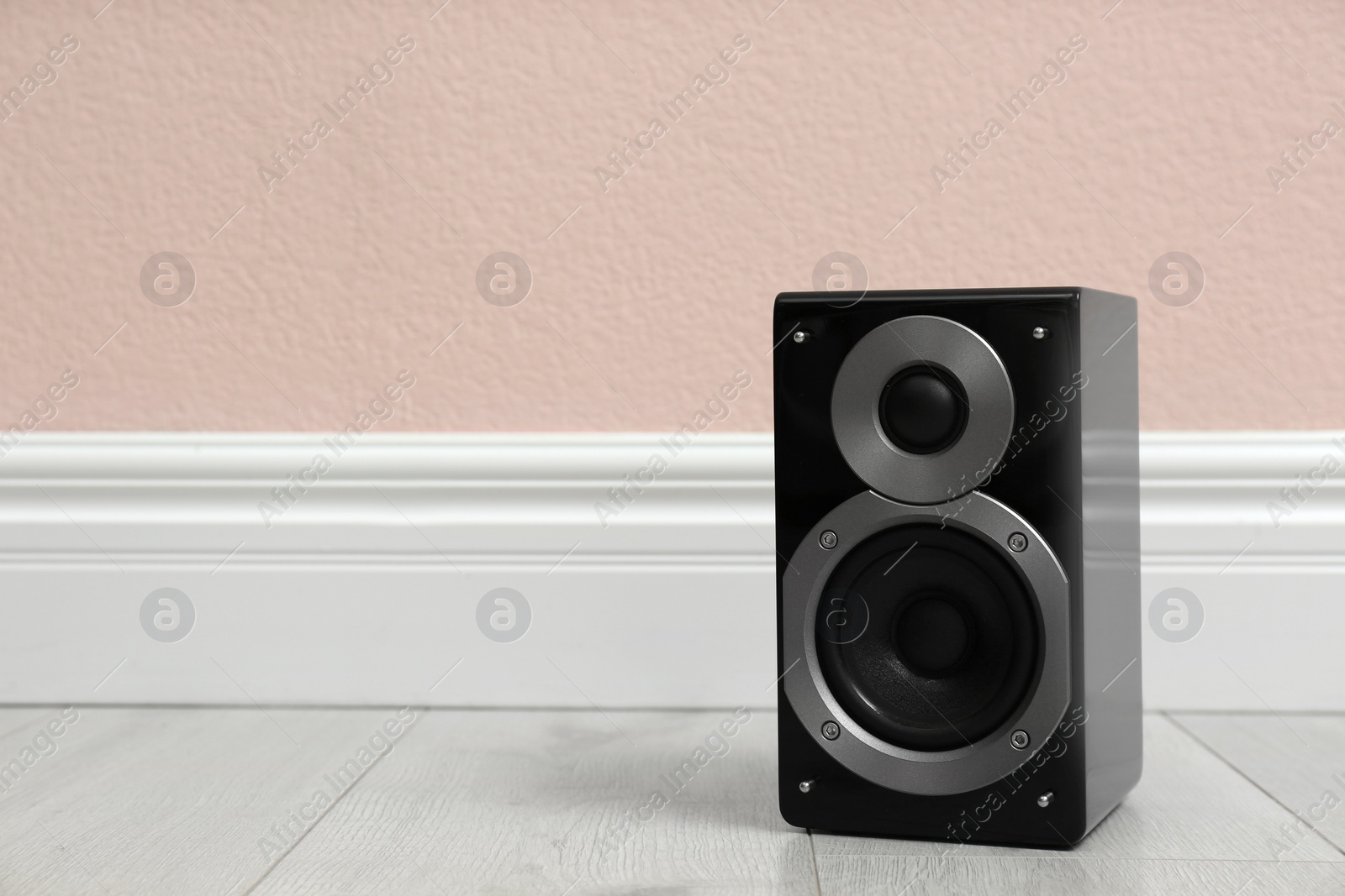 Photo of Modern powerful audio speaker on floor near pink wall. Space for text