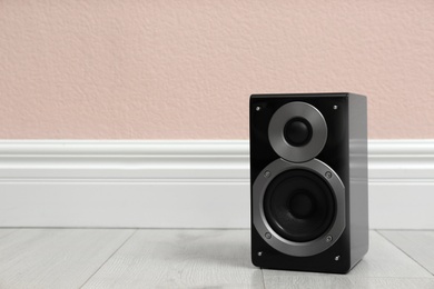 Photo of Modern powerful audio speaker on floor near pink wall. Space for text