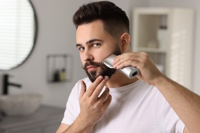 Handsome young man trimming beard at home