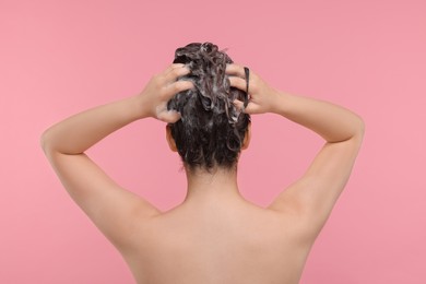 Photo of Woman washing hair on pink background, back view