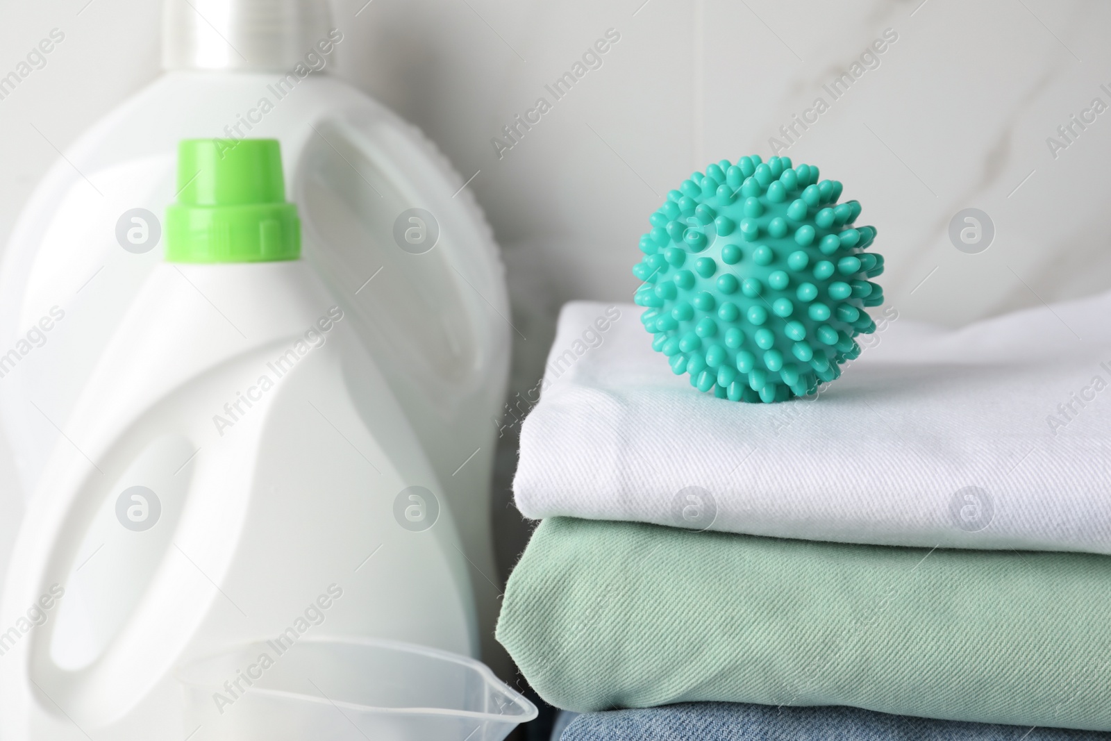 Photo of Turquoise dryer ball on stacked clean towels near laundry detergents