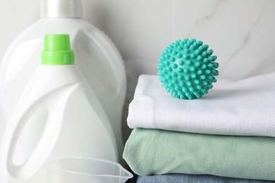 Photo of Turquoise dryer ball on stacked clean towels near laundry detergents