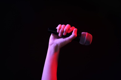 Woman holding microphone on black background, closeup