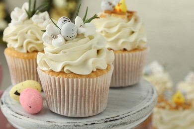 Tasty Easter cupcakes with vanilla cream and candies on cake stand, closeup