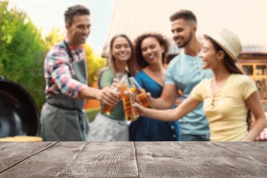 Image of Empty wooden table and blurred view of friends with drinks near barbecue grill outdoors
