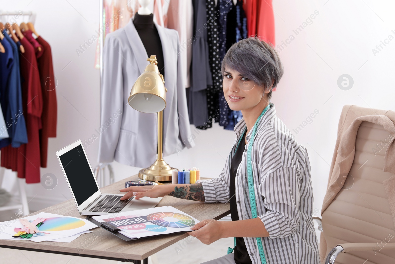 Photo of Beautiful young stylist working with laptop in studio. Trendy clothes