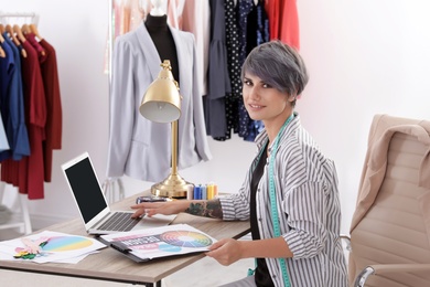 Beautiful young stylist working with laptop in studio. Trendy clothes