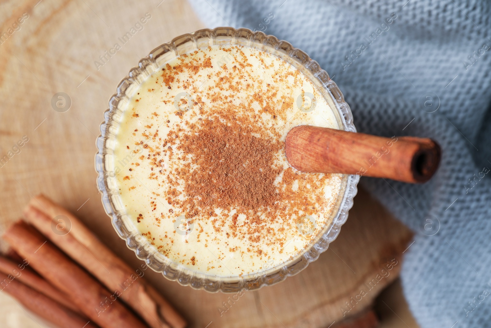 Photo of Glass of delicious eggnog with cinnamon on wooden table, flat lay