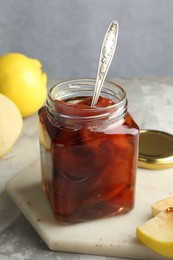 Photo of Tasty homemade quince jam in jar, spoon and fruits on grey textured table