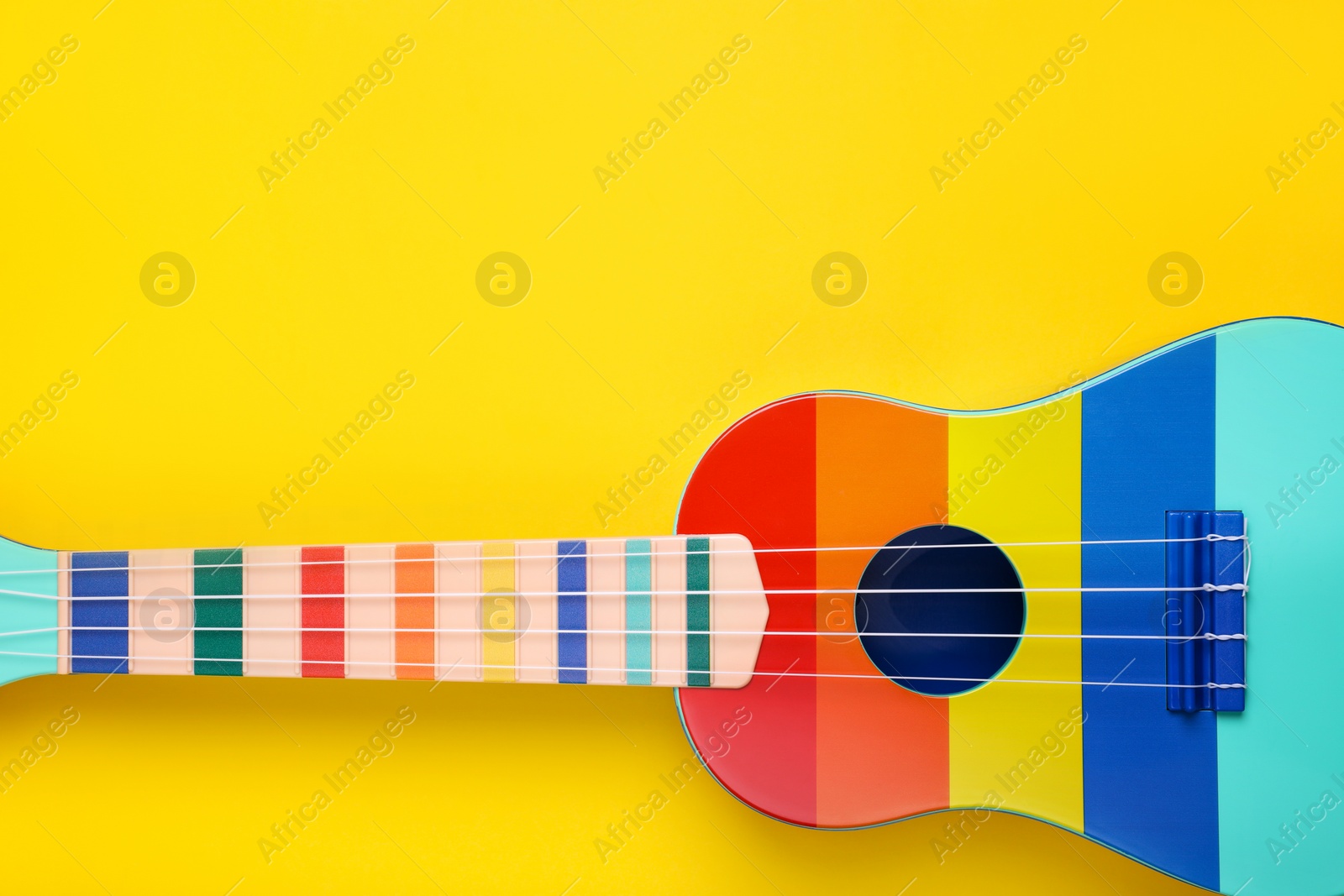 Photo of Colorful ukulele on yellow background, top view with space for text. String musical instrument