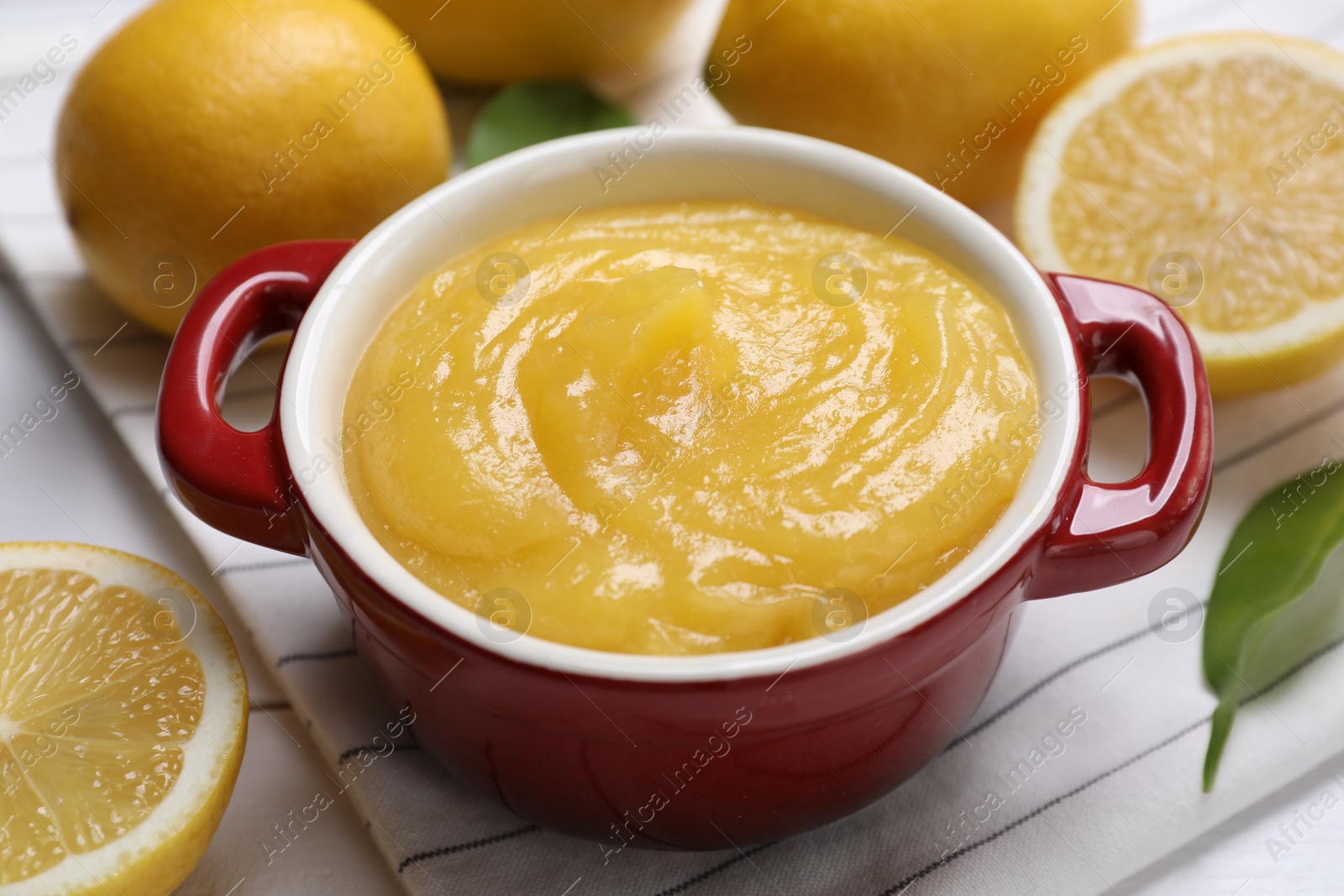 Photo of Delicious lemon curd in bowl and fresh citrus fruits on table, closeup