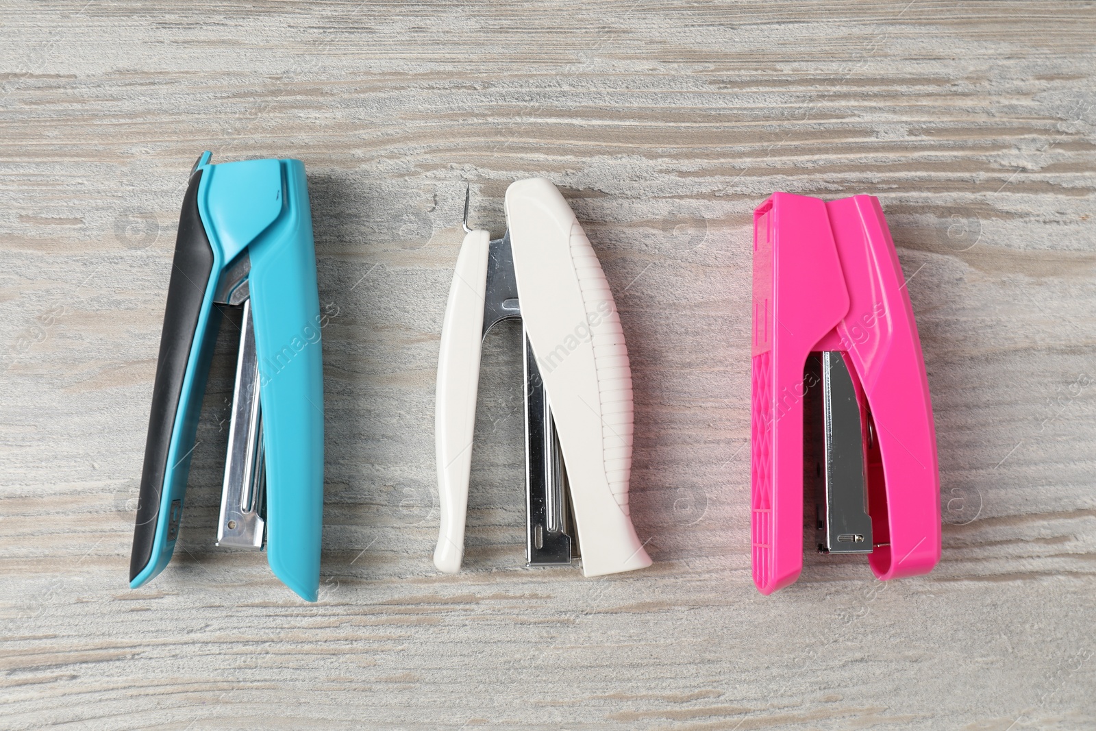 Photo of Color staplers on wooden table, flat lay