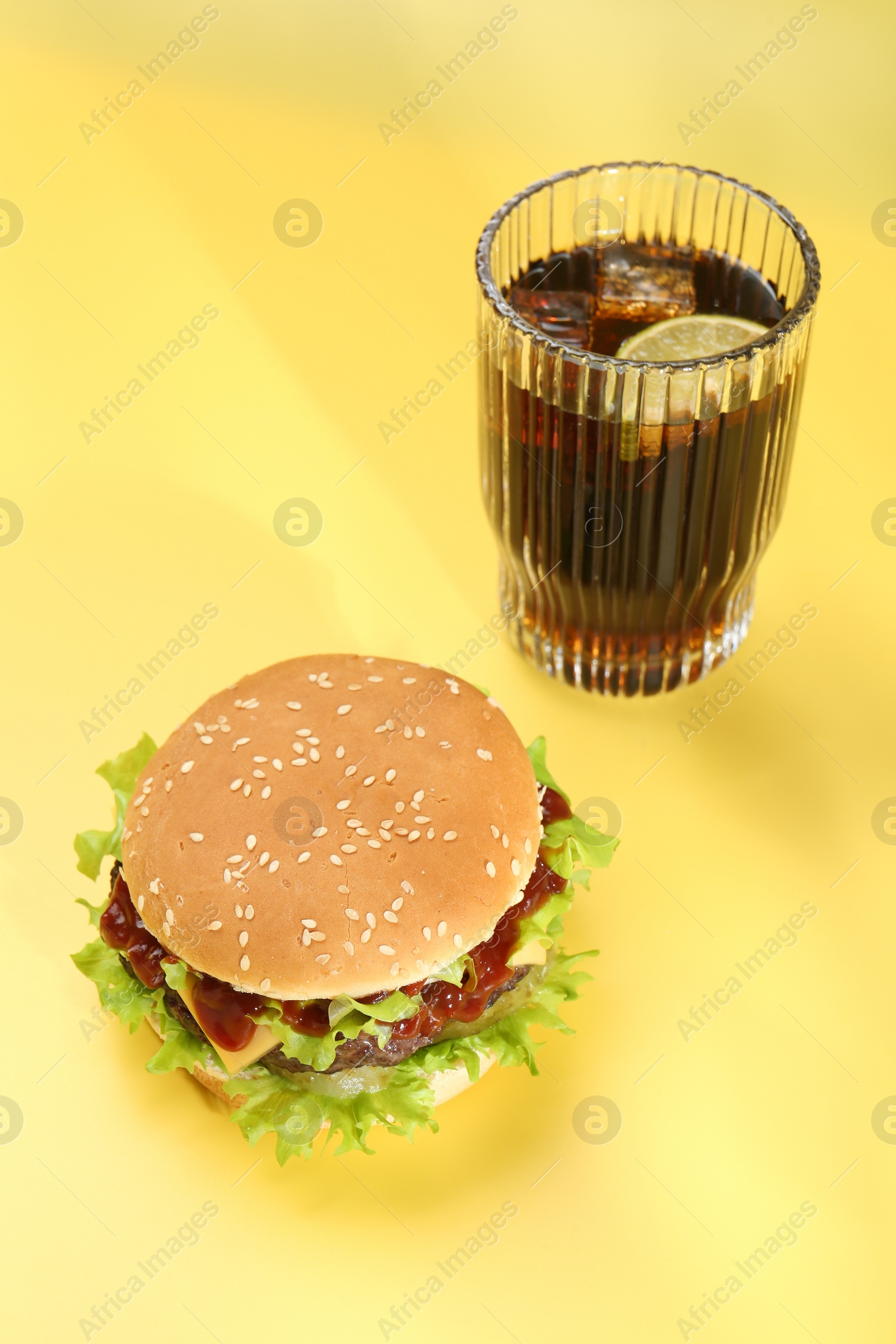 Photo of Burger with delicious patty and soda drink on yellow background