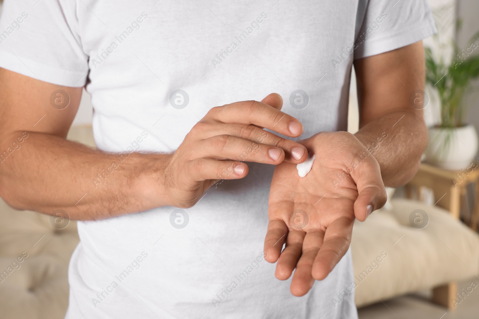 Photo of Man applying cream onto hand at home, closeup