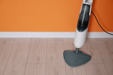 One modern steam mop on floor near orange wall, space for text