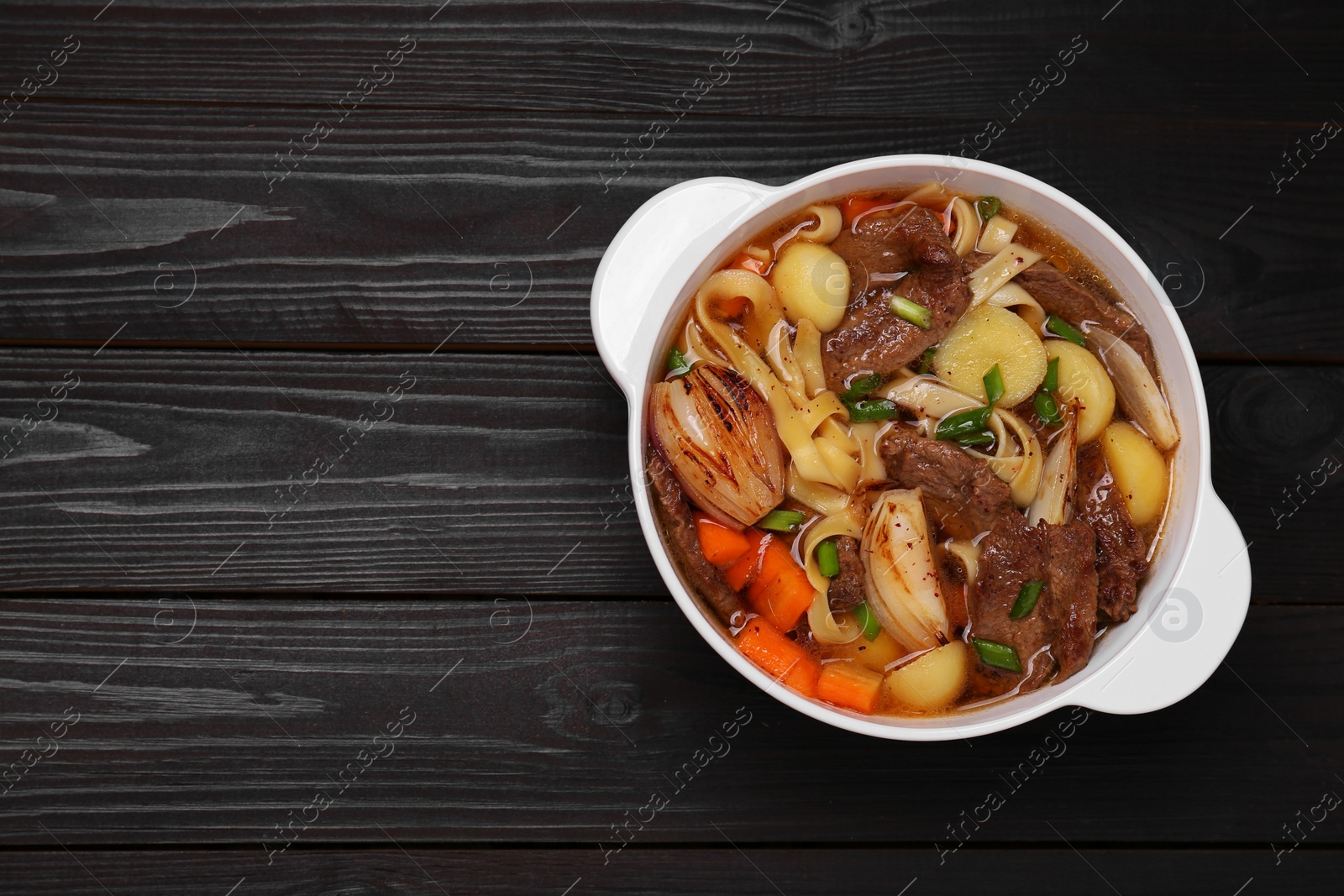 Photo of Pot of delicious vegetable soup with meat, noodles and ingredients on black wooden table, top view. Space for text