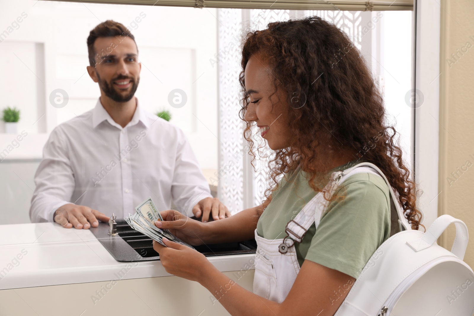 Photo of African American woman with money at cash department window in bank. Currency exchange