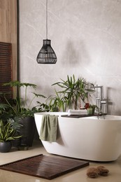 Modern white tub and beautiful green houseplants in bathroom. Interior design